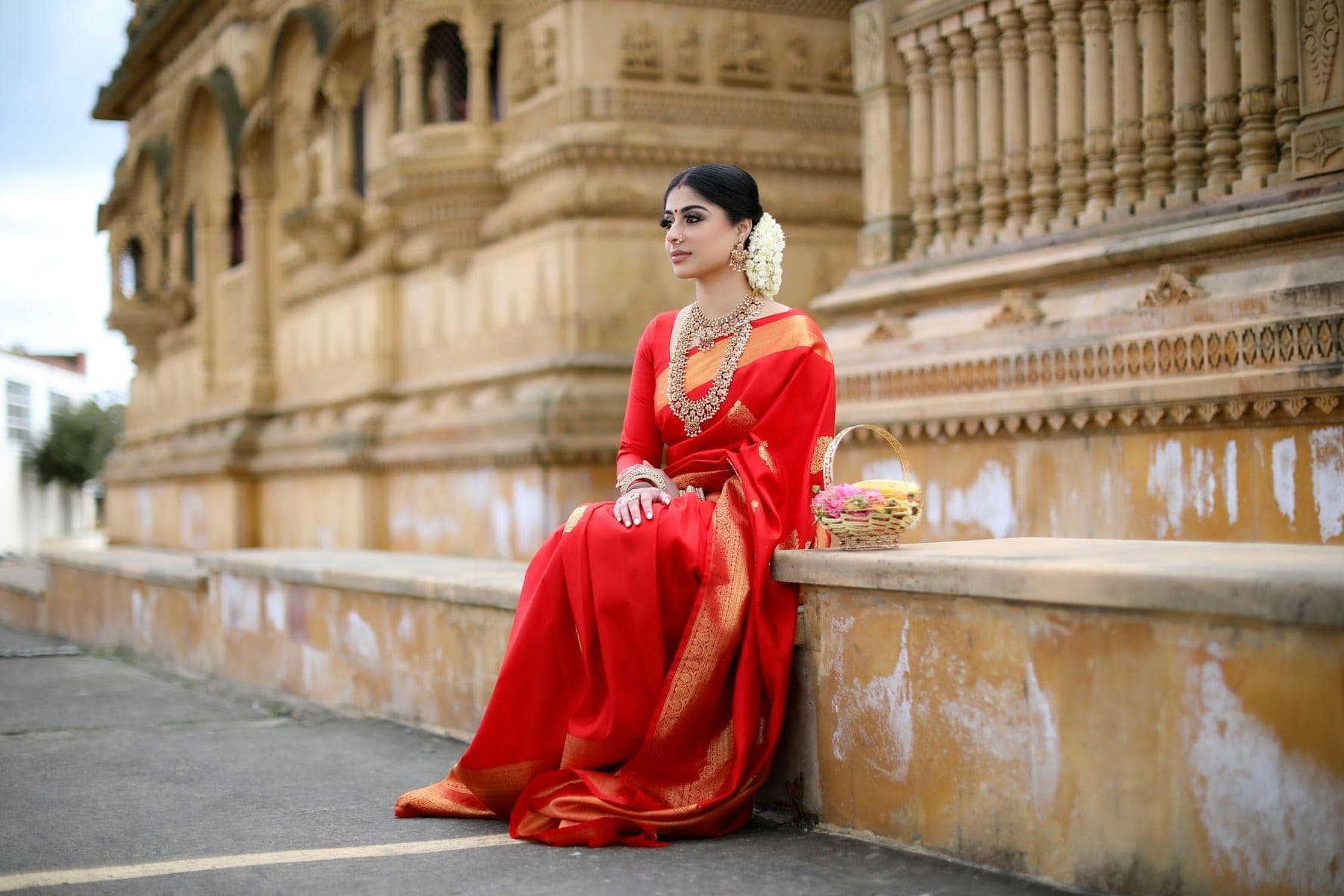 Woman in a red saree seated on carved sandstone steps