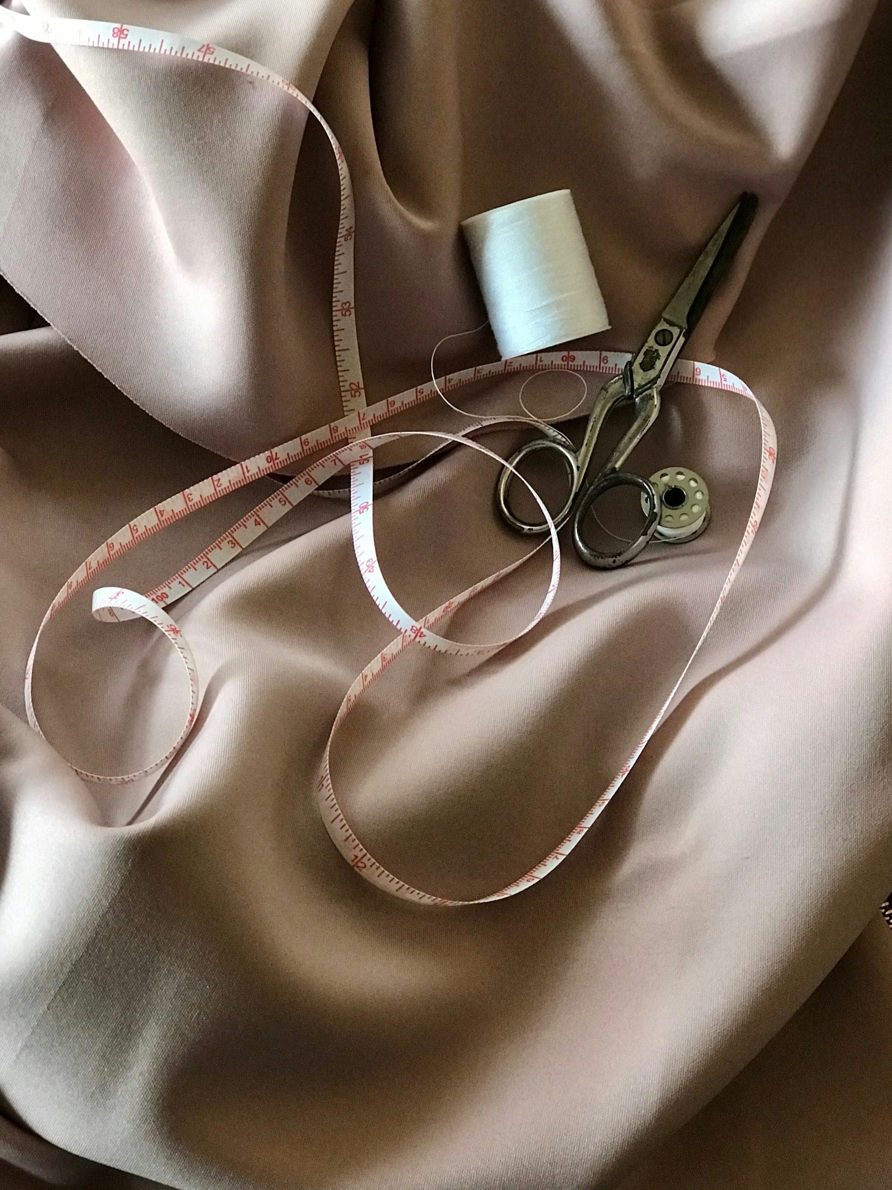 Measuring tape, scissors and thread on champagne silk