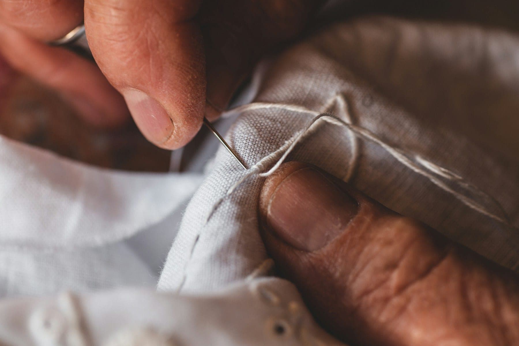 Fingers guiding a needle through ivory fabric